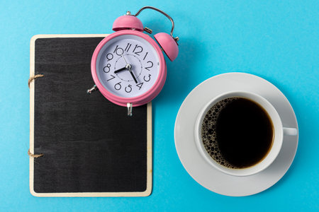Creative layout made with cup of coffee and alarm clock on blue background. Minimal time concept.の写真素材