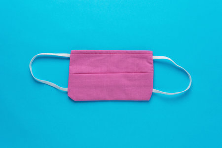 Pink medical face mask on blue background. Minimal Coronavirus outbreak. Pandemic concept.
