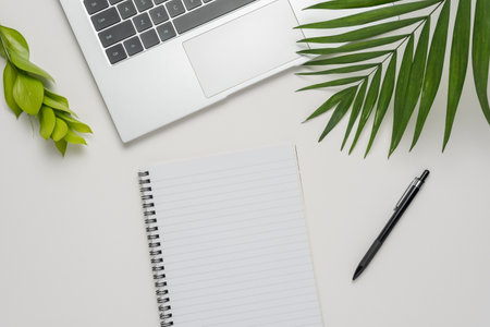 Workspace with blank notebook, laptop, office supplies and green leaves on white background.の写真素材
