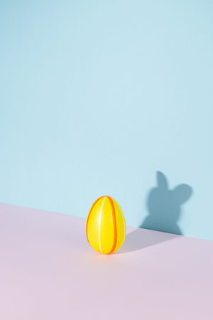 Easter egg with shadow in the shape of bunny or rabbit on pastel pink and blue background. Minimal...