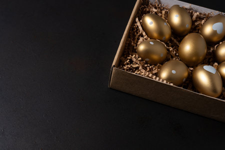 Golden eggs in paper box on dark table.の写真素材