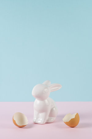 Easter bunny or rabbit with a broken egg shell. Minimal pastel pink and blue Easter holiday concept.の写真素材