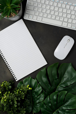 Flat lay, top view office table desk. Workspace with blank notebook, keyboard, office supplies and green leaves on black background.の写真素材