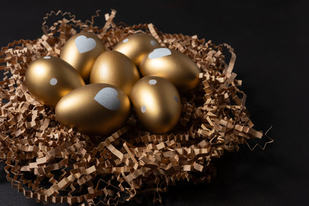 Gold eggs in paper nest on black background.の写真素材