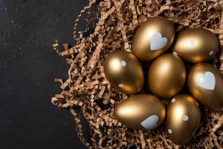 Golden eggs in paper nest on dark table.