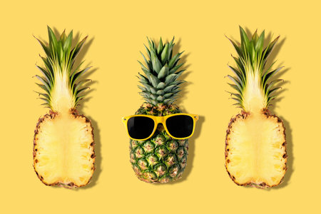 Fresh pineapples with sunglasses on yellow background. Creative summer concept.