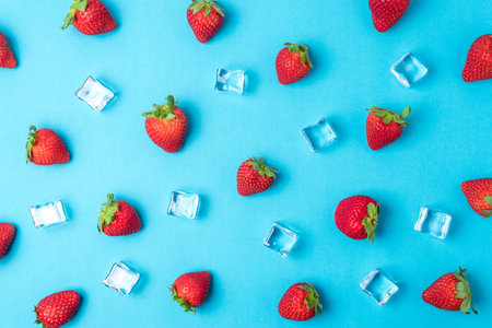 Colorful pattern made of strawberries with ice cubes on blue background. Minimal summer concept.の写真素材