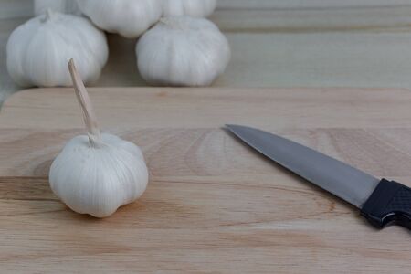 Fresh garlic, placed on a brown wood cutting board and knifeの写真素材