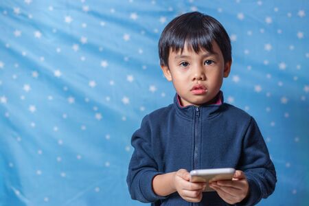 A boy standing with a smartphone and looking Isolated from the blue background with star patternsの写真素材