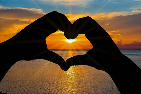 The shadow of the heart-shaped hands clasped with the sunset sky as the backgroundの写真素材