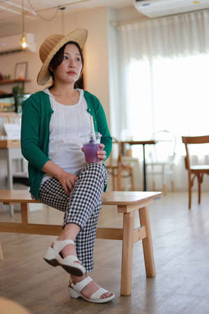 Asian pregnant women in white-green shirts Scotch Kewa Sit on a wooden chair to relax in a modern home holding a glass of juice. With indoor and portraitの写真素材