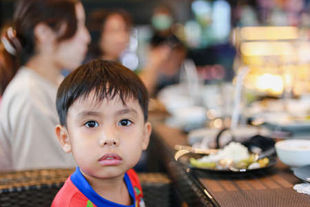 Close up portrait in front of a red shirt boy sitting view at dining table bokeh blur background in restaurantの写真素材