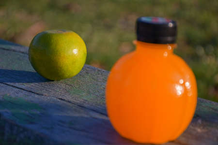 Close-up selection of fresh citrus fruits on wooden floor and blurry lawn background and blurry orange juice bottle foreground and copy space.の写真素材