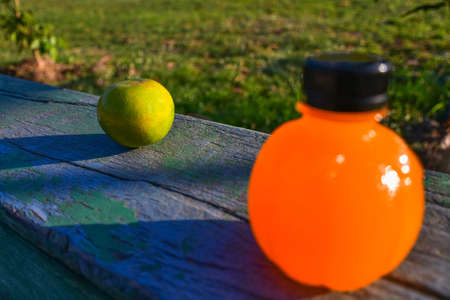 Shiny orange fruit on wooden background with blurry plastic orange juice bottle. Blurred lawn background with copy spaceの写真素材