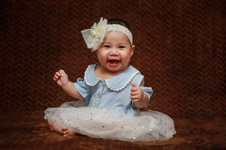 Portrait Asian looking toddler wearing a blue shirt and white bow headband indoors.
sitting happy laughing brown backgroundの写真素材