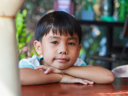 Close up portrait Cute black haired Asian boy aged 8-10 years old looking up smiling happy expression wearing white shirt and the indoor posing of an innocent boyの写真素材
