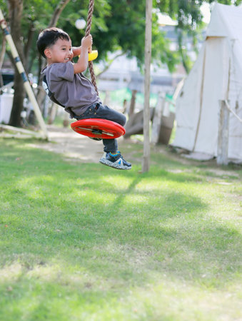Adventure boy sitting moving red swing flying excitement under the tree on the green lawn copy spaceの写真素材