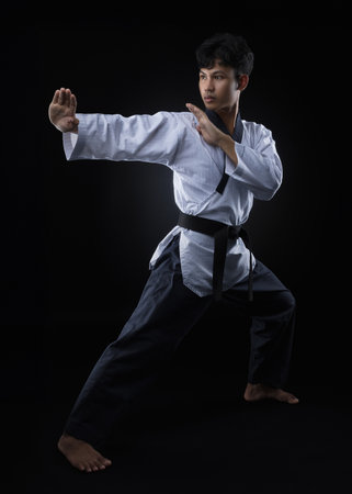 A black belt taekwondo athlete poses and demonstrates fighting moves against a black background Conceptual portraits of athletes for educationの写真素材