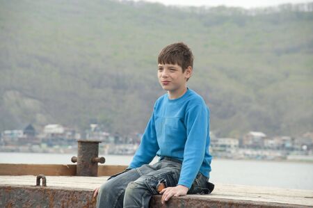 The boy sitting near the sea on a mooring for boatsの写真素材