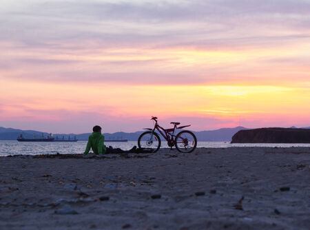 young man sitting on the beach at sunsetの写真素材