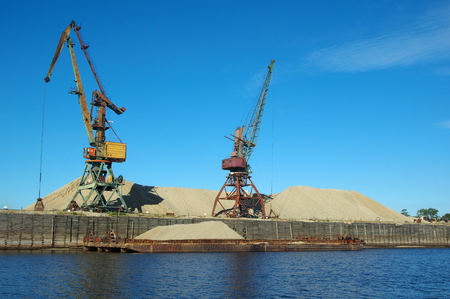 Loading sand with the help of a crane on a barge on the water and sky background of yellow sand.の写真素材