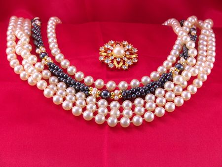 White and black pearl chokers on red fabric with pearl broochの写真素材