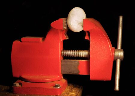 An egg held in a vise cracking under pressureの写真素材