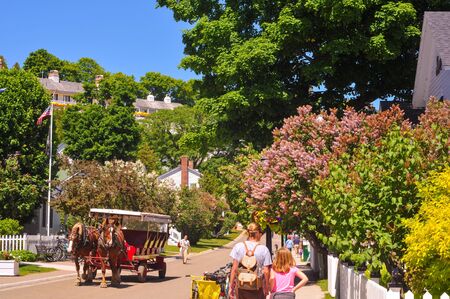 MACKINAC ISLAND, MI - JUNE 26, 2014: A horse-drawn cab and pedestrian visitors amble along flowery Market Street on a sunny summer day.のeditorial素材