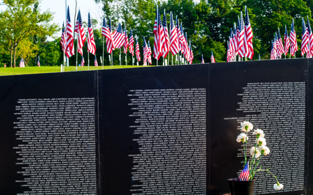TWINSBURG, OH, USA - JULY 4, 2015: A field of flags is seen above a section of a replica Vietnam Memorial Wall, on tour with the Cost of Freedom tribute, a traveling veterans-based exhibitのeditorial素材