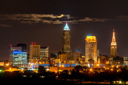 Brightly lit Cleveland Ohio under a full moon rising through a wisp of cloudsの写真素材