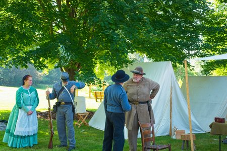 TWINSBURG, OH - JUNE 30, 2018: A group of Civil War reenactors converse by tents and displays in the shade during an all-day history event at the Twinsburg Public Library.のeditorial素材