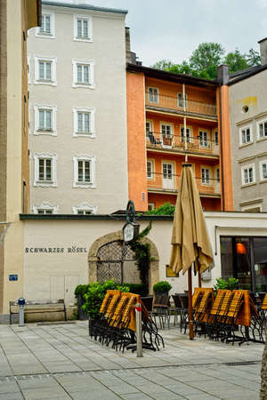 SALZBURG, AUSTRIA - MAY 26, 2019: Street-level view of the front gate and facade of the Schwarzes RÃ¶ssl, an old hotel that now serves as a student dormitory, with outdoor seating for a neighboring cafe.のeditorial素材