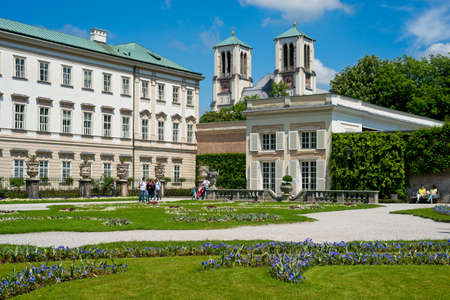 SALZBURG, AUSTRIA - MAY 26, 2019: Visitors enjoy the gardens of the Mirabell Palace (Schloss Mirabell) in late spring with the towers of the AndrÃ¤kirche rising behind.のeditorial素材