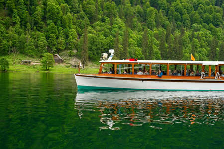 UPPER BAVARIA, GERMANY - MAY 27, 2019: An excurion boat on Bavariaâs KÃ¶nigssee glides past a rustic shelter under steep forested slopes; the water gets its green color from minerals.のeditorial素材