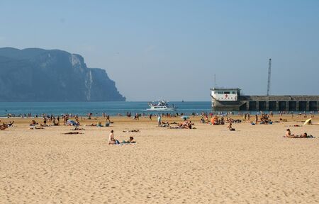 Laredo, Cantabria, EspaÃ±a; 08/07/2008: Laredo beach, with tourists in the sand. A ship enters the old port and the building of the red crossのeditorial素材