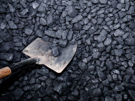 Metal shovel with wooden handle collecting carbon stones from a pileの写真素材
