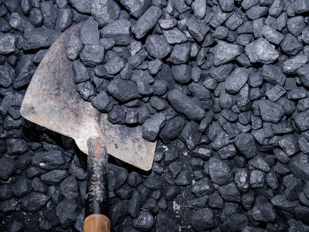Metal shovel with wooden handle collecting carbon stones from a pileの写真素材