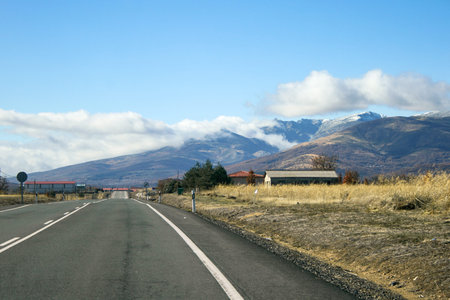 Road with road signs and snowy mountains with clouds around background with a nice blue sky