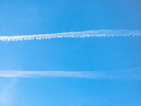 Two White streaks plans leave behind like artificial clouds. Blue sky backgroundの写真素材