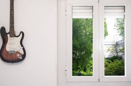 Photograph of a guitar and a window overlooking the street to represent the idea that during the confinement caused by the Covid-19 it is a good time to recover or learn hobbies such as music.の写真素材