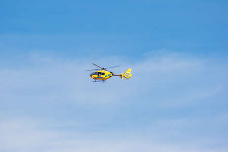 San Sebastian de los Reyes, Madrid, Spain; 02/05/2020: Yellow EC-MZR helicopter with blue details and a front camera flying over a blue sky with cloudsのeditorial素材