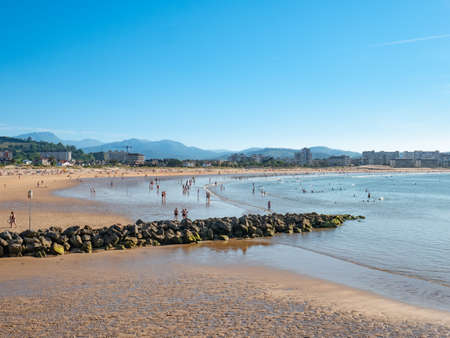 Laredo, Cantabria, Spain; 04/07/2020: Tourists and bathers enjoying Salve de Laredo beach during a beautiful blue summer day at low tide behind the rocksのeditorial素材