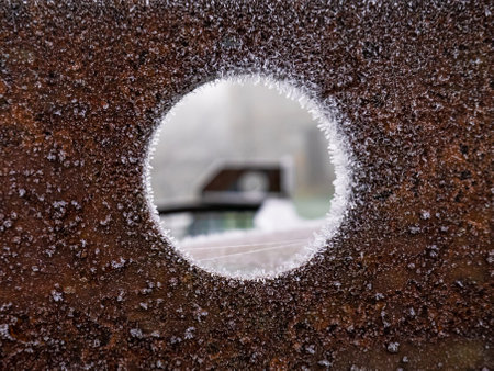 Rusty sheet metal with a hole in the center completely frozen around its circumference, revealing out-of-focus machineryの写真素材