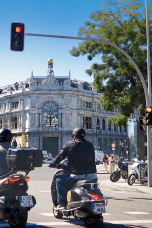 Madrid, Spain; September 21st, 2021: Motorcyclist standing with a classic looking motorcycle and with an open face helmet, at a red traffic light in front of the bank of Spain buildingのeditorial素材