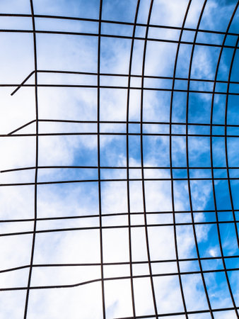 Iron fence made up of rusty metal bars outdoors with a blue sky in the background and large white cloudsの写真素材