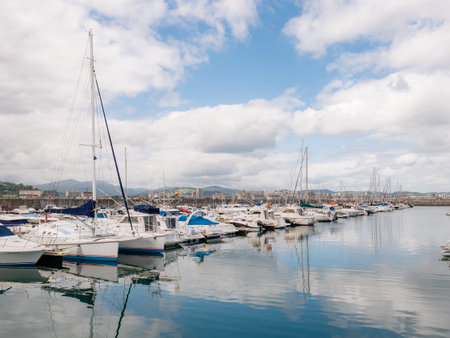 Laredo, Cantabria, Spain; 08-17-2021: Sailboats and sports boats moored at the moorings of the Laredo marina in a row, the clouds in the sky are reflected in the sea giving a rough appearanceのeditorial素材