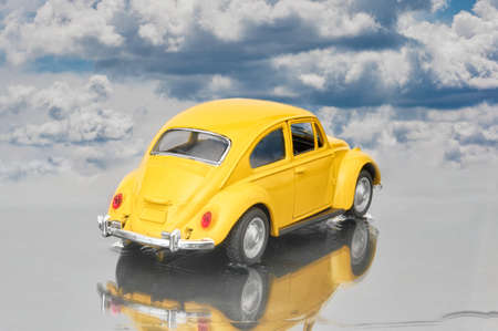 MadridSpain; 03-17-2022: Model of a yellow Beetle seen from behind parked in a puddle and the lights on, we can see its reflection in the puddle and a nice cloudy sky behindのeditorial素材