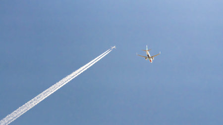 Two commercial airplanes flying in clear blue sky, one leaving white contrails