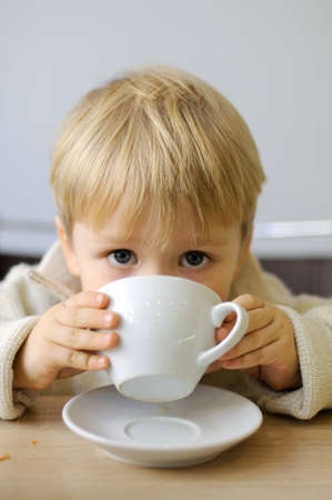 Little boy drinking from a cup tea in a cafeの写真素材