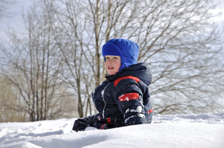 A little boy on a big snowdrift in winter snow throws.